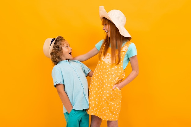 Dos amigas pelirrojas con sombreros de verano se miran en un amarillo