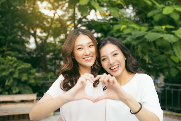 Dos amigas de pie en un abrazo y formando forma de corazón con las manos en la naturaleza. Concepto de amistad