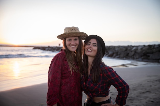 Dos amigas en la playa de vacaciones sonriendo durante la puesta de sol