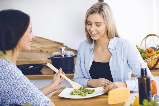 Dos amigas prueban nuevas recetas de deliciosas ensaladas frescas mientras se sientan en la mesa de la cocina Concepto de cocina vegetariana