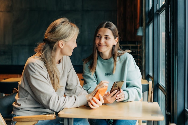 Foto dos amigas sentadas en un café viendo medios en línea en el teléfono y riendo