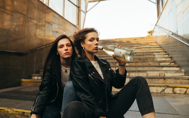 Dos amigas sentadas en las escaleras en el metro, bebiendo vino de una botella