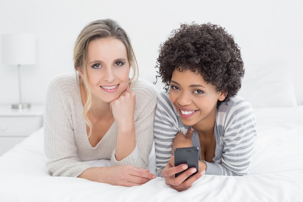 Dos amigas sonrientes leyendo mensajes de texto en la cama