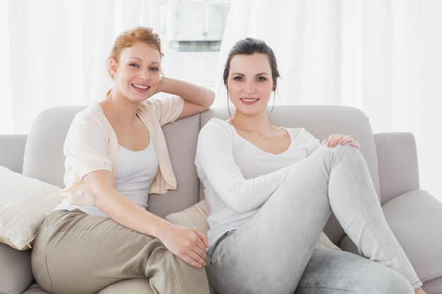 Dos amigas sonrientes, sentado en el sofá en la sala de estar