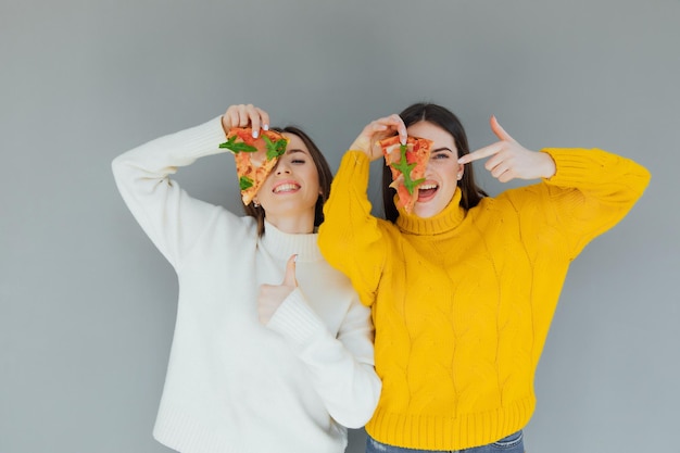 Dos amigas sosteniendo porciones de pizza. Jóvenes divirtiéndose cenando.