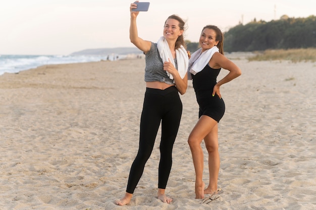 Foto dos amigas tomando un selfie en la playa mientras hace ejercicio