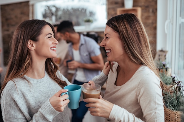 Dos amigas en traje casual hablando y bebiendo té y café.