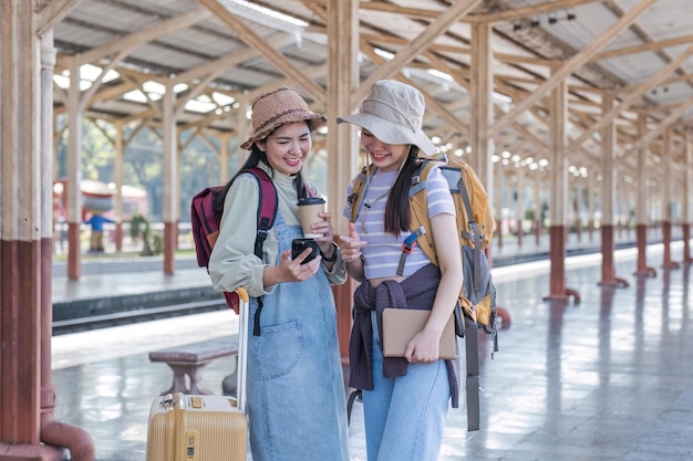 Foto dos amigas turistas asiáticas están en la estación de tren esperando el tren para viajar a la