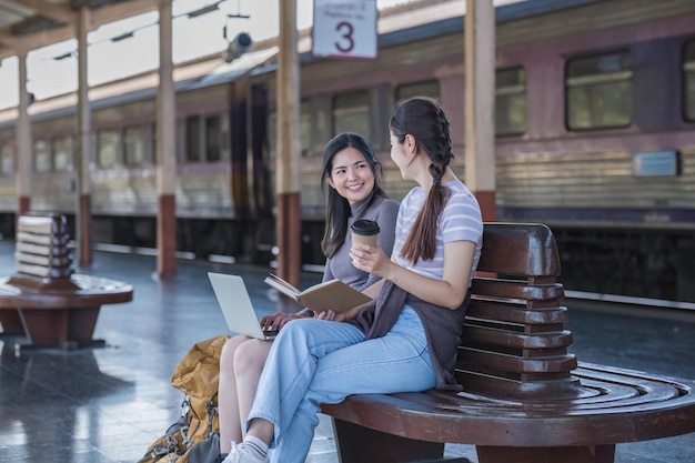 Foto dos amigas turistas asiáticas están en la estación de tren esperando el tren para viajar a la