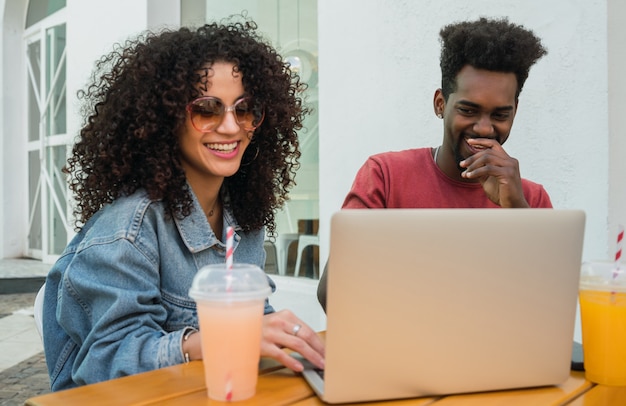 Dos amigos afro usando laptop en una cafetería.