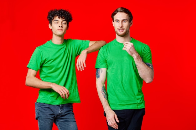 Dos amigos alegres en camisetas verdes alegría de comunicación fondo rojo