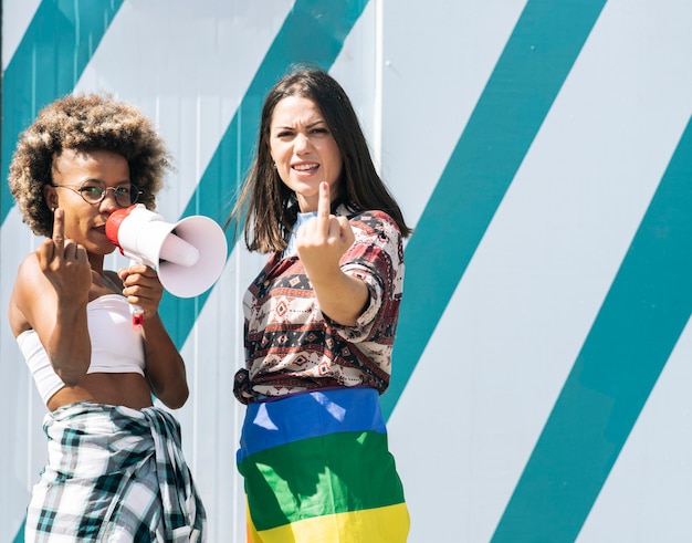 Dos amigos con una bandera LGBT hacen un gesto de sacar los dedos