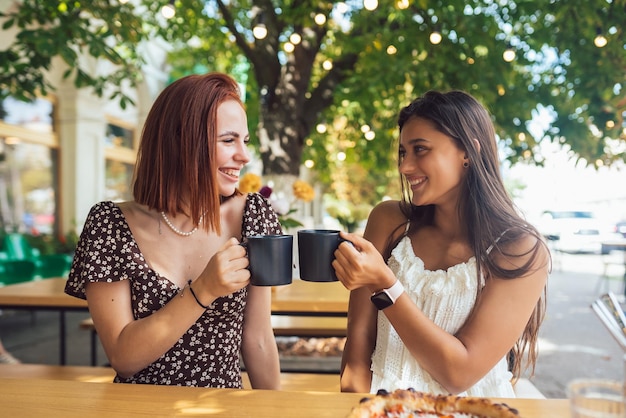 Dos amigos bebiendo café mujeres tintineando con tazas de café