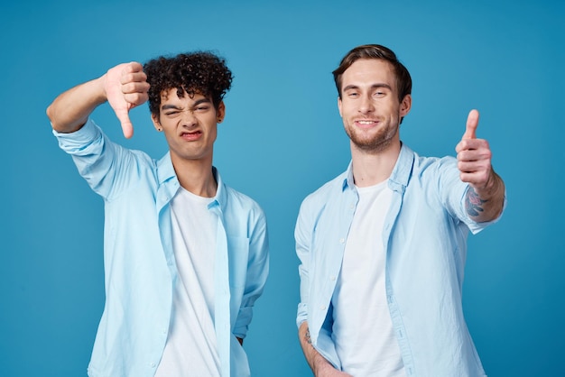 Dos amigos con camisetas idénticas y una camiseta gesticulando con las manos sobre un fondo azul.