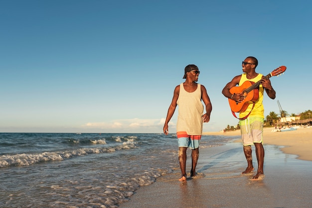 Dos amigos cubanos divirtiéndose en la playa con su guitarra. Concepto de amistad.