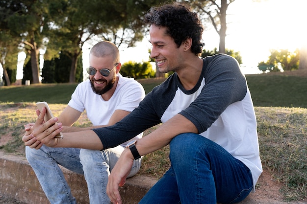 Dos amigos divirtiéndose con el móvil en el parque al atardecer