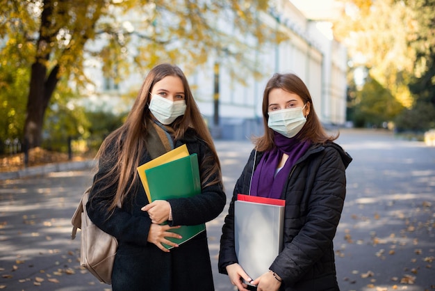 Foto dos amigos de estudiantes universitarios en máscaras médicas que van a clases por la mañana