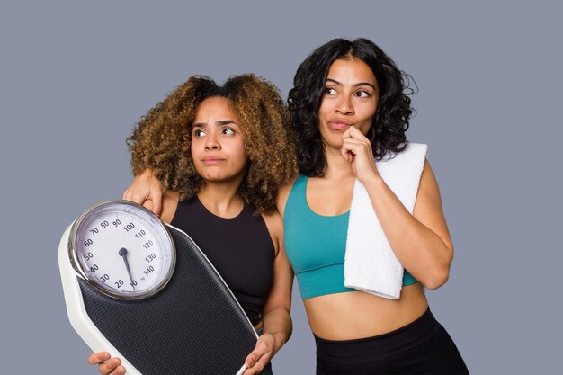 Dos amigos étnicamente diversos se dirigen juntos al gimnasio motivados y centrados en el fitness. Uno sostiene una báscula que simboliza la dedicación a la dieta y la disciplina.