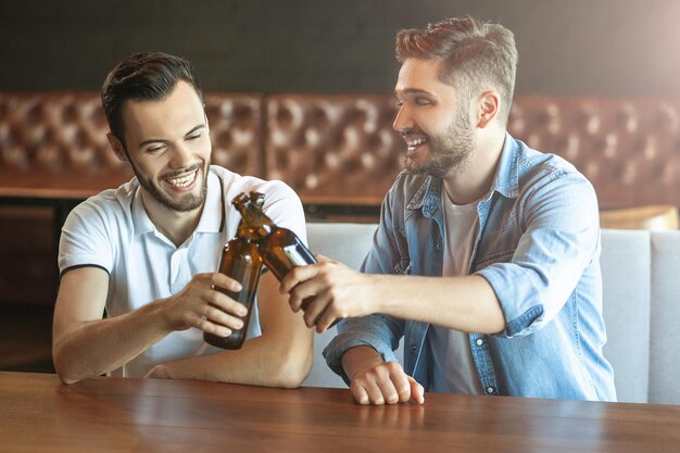 Dos amigos felices animando con botellas de cerveza en el café