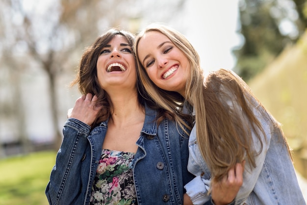 Dos amigos felices de las mujeres jovenes que abrazan en la calle.