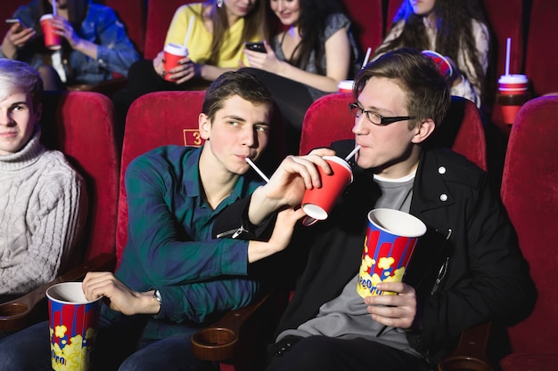 Dos amigos, hermanos beben a través de un tubo en el cine.