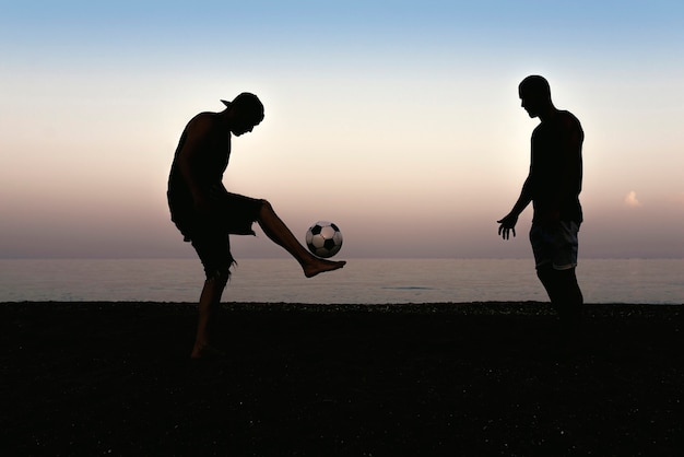 Dos amigos jugando al fútbol en la playa.