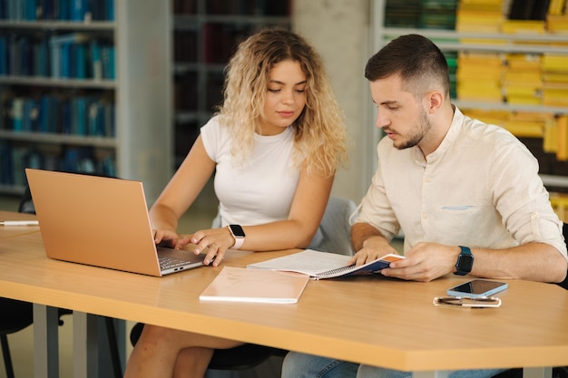 Dos amigos, niño y niña, estudian en la biblioteca de la universidad Vista posterior de estantes con libros Preparándose para el examen