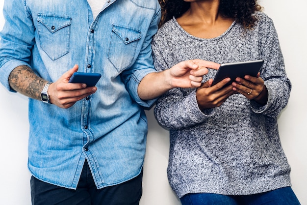 Dos amigos se relajan usan la tecnología juntos de teléfonos inteligentes que comprueban las aplicaciones sociales en la pared de la pared.