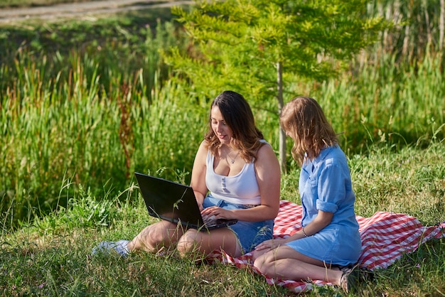 Dos amigos sentados en un parque con una computadora portátil.