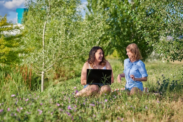 Dos amigos sentados en un parque con una computadora portátil.