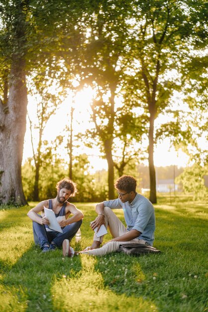 Dos amigos sentados en un parque con dispositivo móvil y papeles.