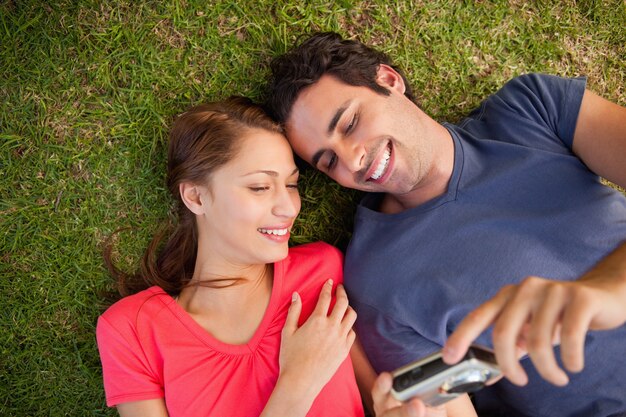 Dos amigos sonriendo mientras mira fotos en una cámara mientras yacen uno al lado del otro en la hierba