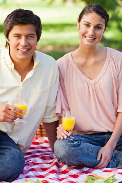 Dos amigos sonriendo mientras sostiene vasos de jugo durante un picnic