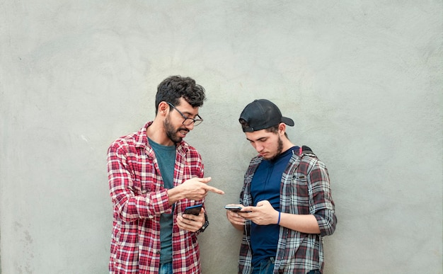 Dos amigos transfiriendo archivos desde sus celulares Dos chicos revisando sus celulares Dos jóvenes comparando sus celulares