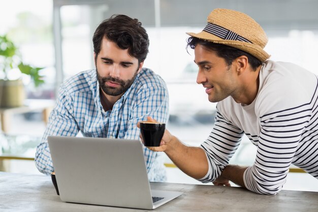 Dos amigos usando laptop mientras tomando una taza de café