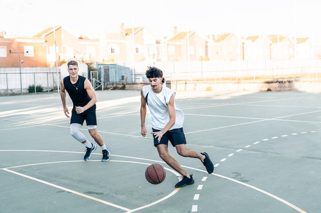 Dos amigos varones corriendo mientras jugaba baloncesto en una cancha al aire libre durante la puesta de sol