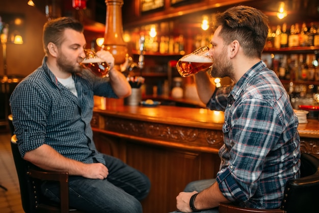 Dos amigos varones sonrientes beben cerveza en el mostrador del pub.