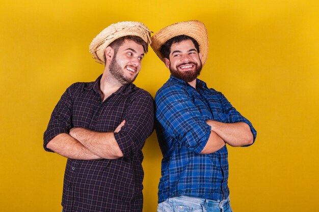 Dos amigos vestidos con ropa típica de la Festa Junina con los brazos cruzados sonriendo