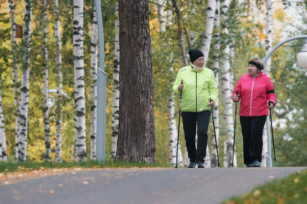 Dos ancianas participan en caminatas escandinavas en el parque