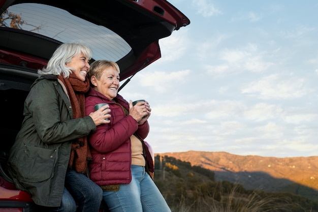Dos ancianas sentadas en el baúl del auto mientras salen a una aventura en la naturaleza