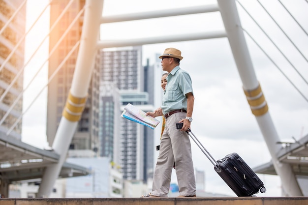 Dos ancianos asiáticos viajando con mapa y equipaje contra el edificio