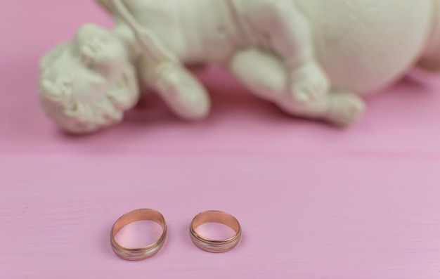 Dos anillos de boda contra la figura caída de un ángel Cupido El concepto de extinción y ruptura de relaciones