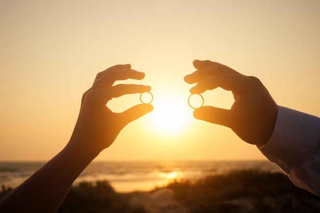 Dos anillos de boda en coral frente al mar al atardecer.