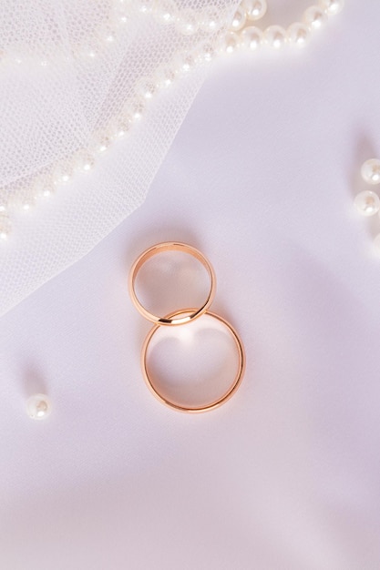 Dos anillos de boda de oro sobre un elegante fondo de satén blanco con un collar de perlas Diseño de fondo de boda vertical para el diseño