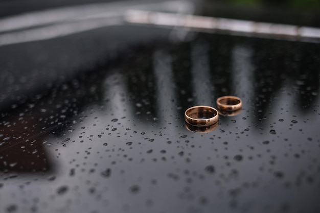 Dos anillos de boda yacen uno encima del otro sobre un fondo oscuro Caen gotas de agua sobre ellos