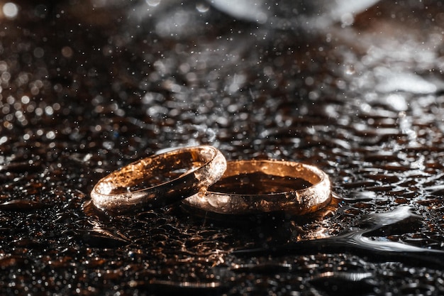 Dos anillos de bodas de oro en gotas de lluvia sobre un fondo húmedo negro