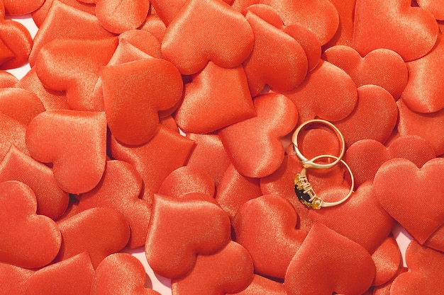 Dos anillos de bodas de oro sobre fondo rojo satinado corazones