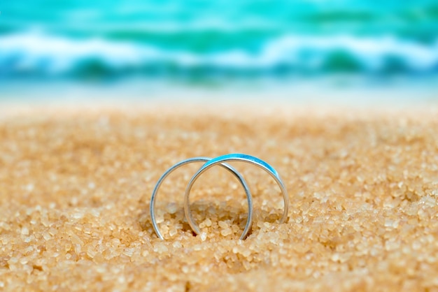 Dos anillos de plata de boda en la arena en el fondo de la playa y el mar