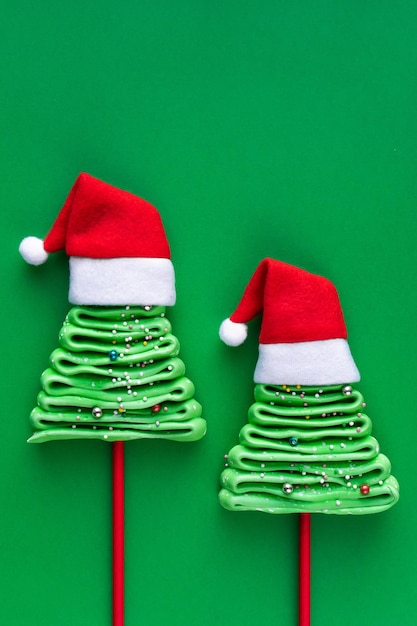 Dos árboles de merengue al estilo de Año Nuevo sobre un fondo verde. Árboles de Navidad en gorros rojos de santa.