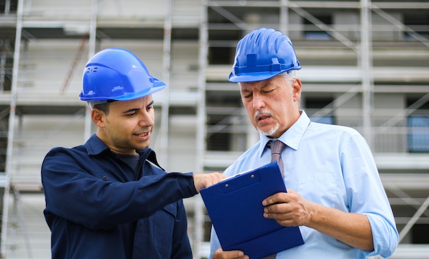 Dos arquitectos desarrolladores que revisan los planes de construcción en el sitio de construcción